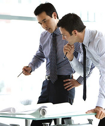 two businessman standing over and studying some forms