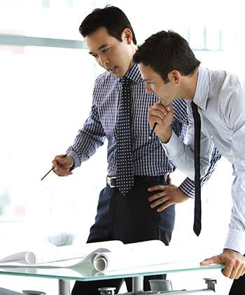 two businessman standing over and studying some forms