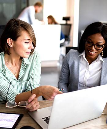 Hoe verlaagt automatisering de kosten?   two women working on a laptop